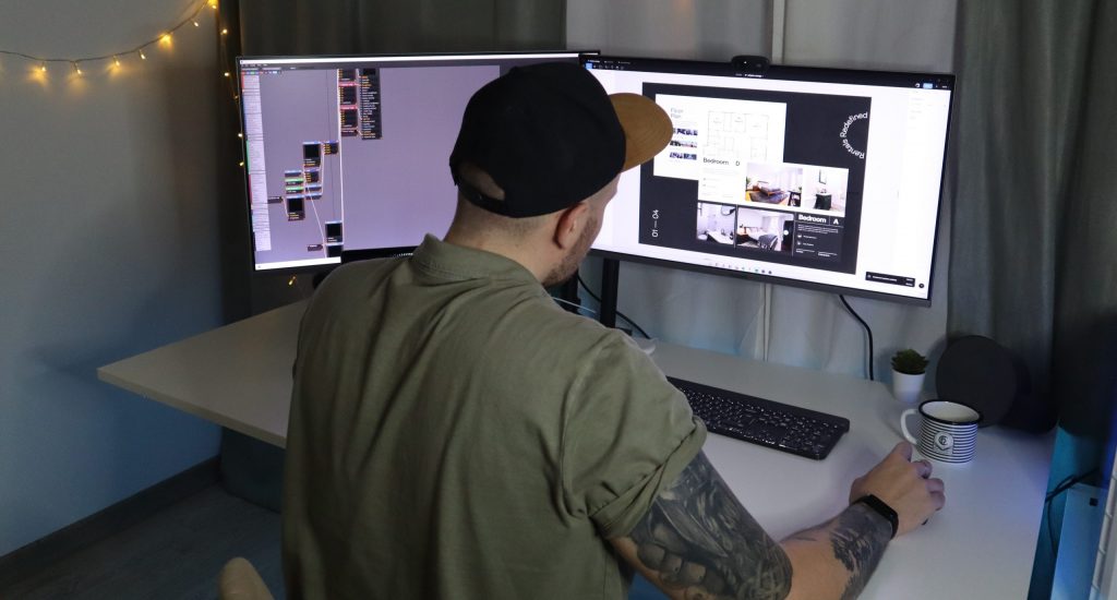 man in green dress shirt and black cap sitting in front of computer