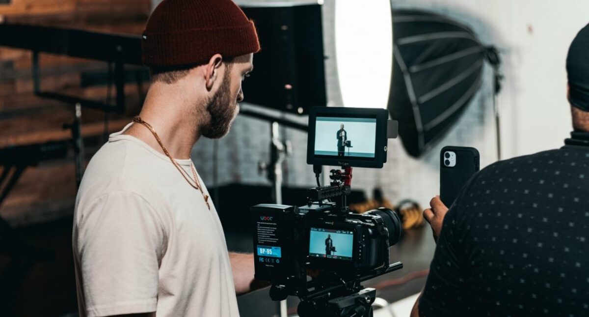 man in white polo shirt standing in front of black video camera