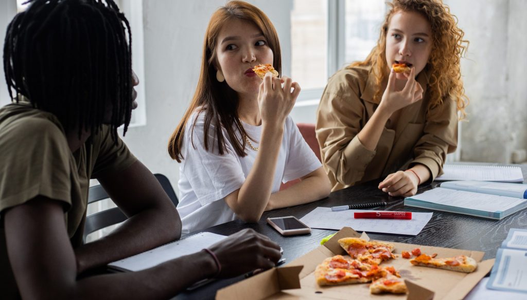 Multiethnic students eating pizza during break in studies