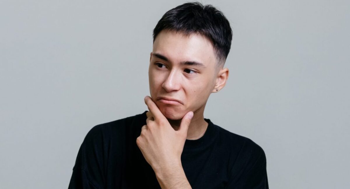 Man in black crew neck shirt thinking with his hand on his chin