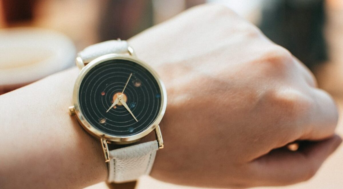 Round gold colored black analog watch with grey leather band