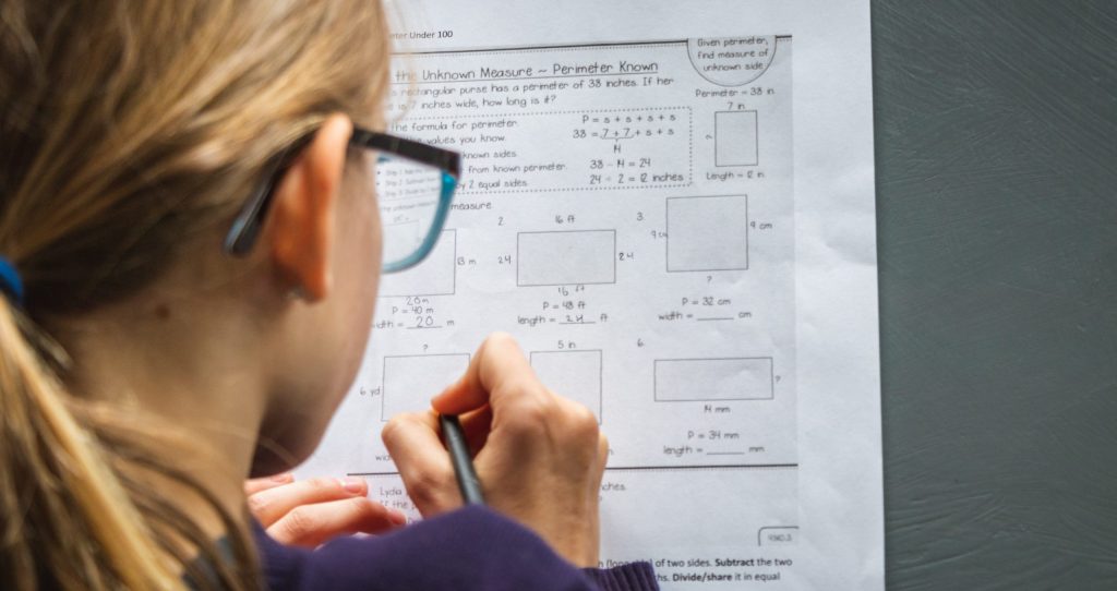 view of young girl with glasses from behind working on school work