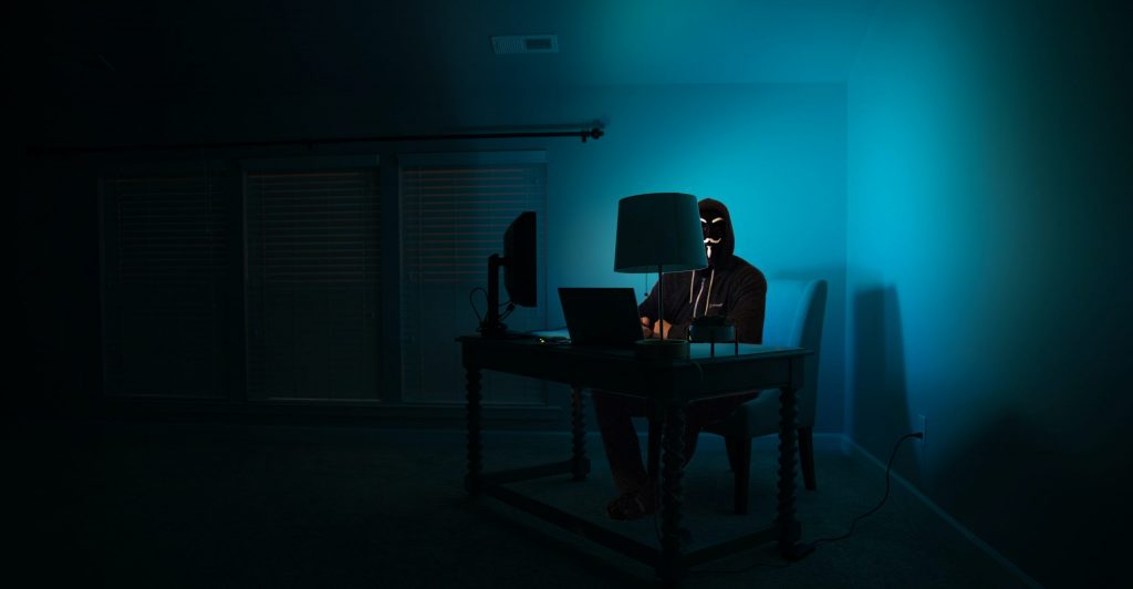 Pictured - a man at a computer disguised as an anonymous hacker wearing a Guy Fawkes mask.