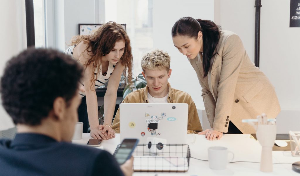 Women standing beside a man using a laptop