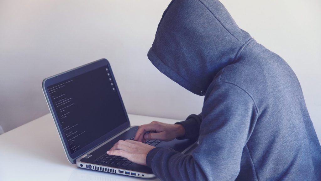 Anonymous hacker with on laptop in white room